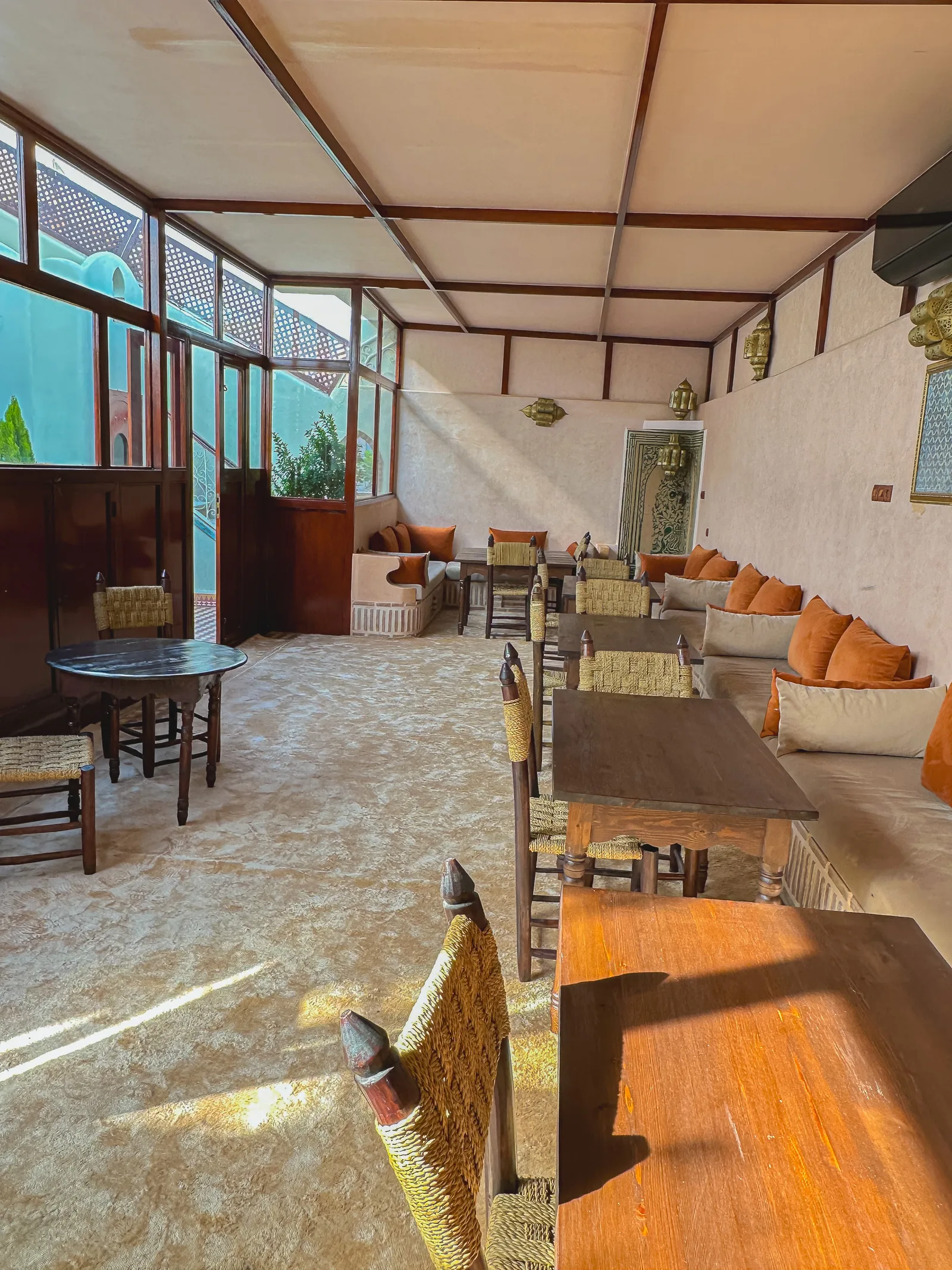 The covered dining room on the second floor of Riad Tasneem: banquettes with terracotta cushions, wooden tables and a glazed front towards the patio skylight
