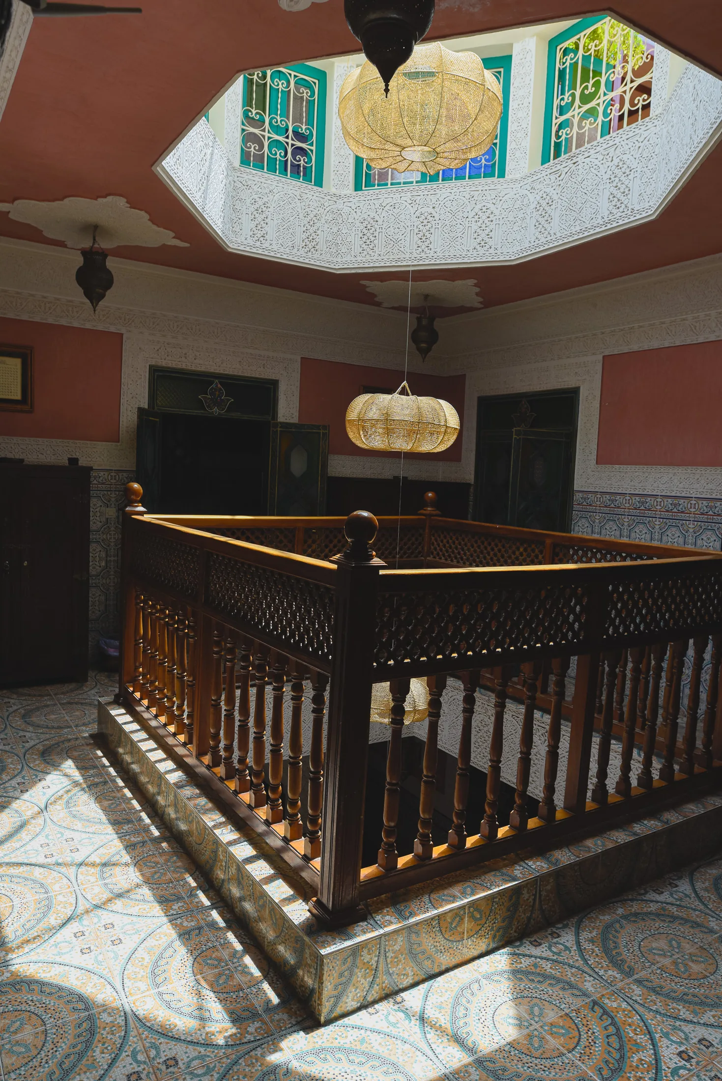 First-floor gallery at Riad Tasneem: carved wooden balustrade around the courtyard opening, octagonal stucco skylight and brass lanterns