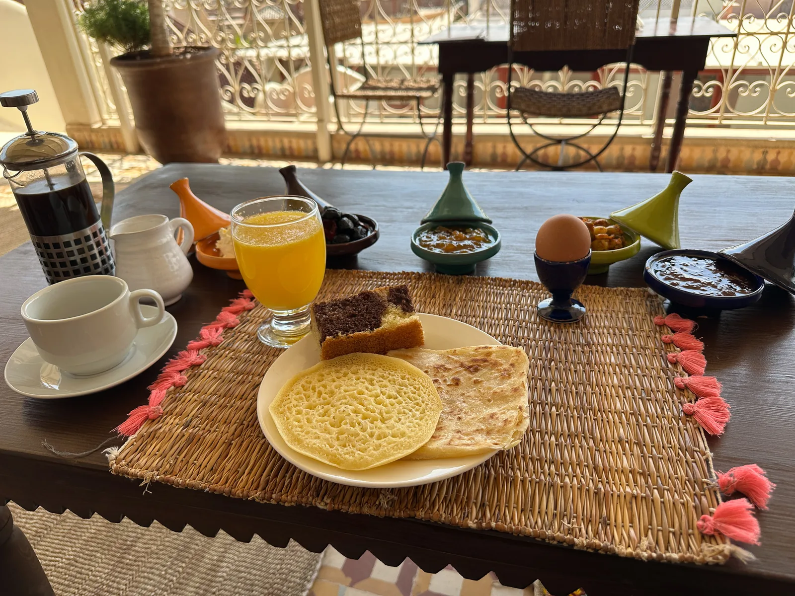 Moroccan breakfast at Riad Tasneem: baghrir and msemen pancakes, marble cake, boiled egg, olives, jams in small tagines, orange juice and coffee on the rooftop