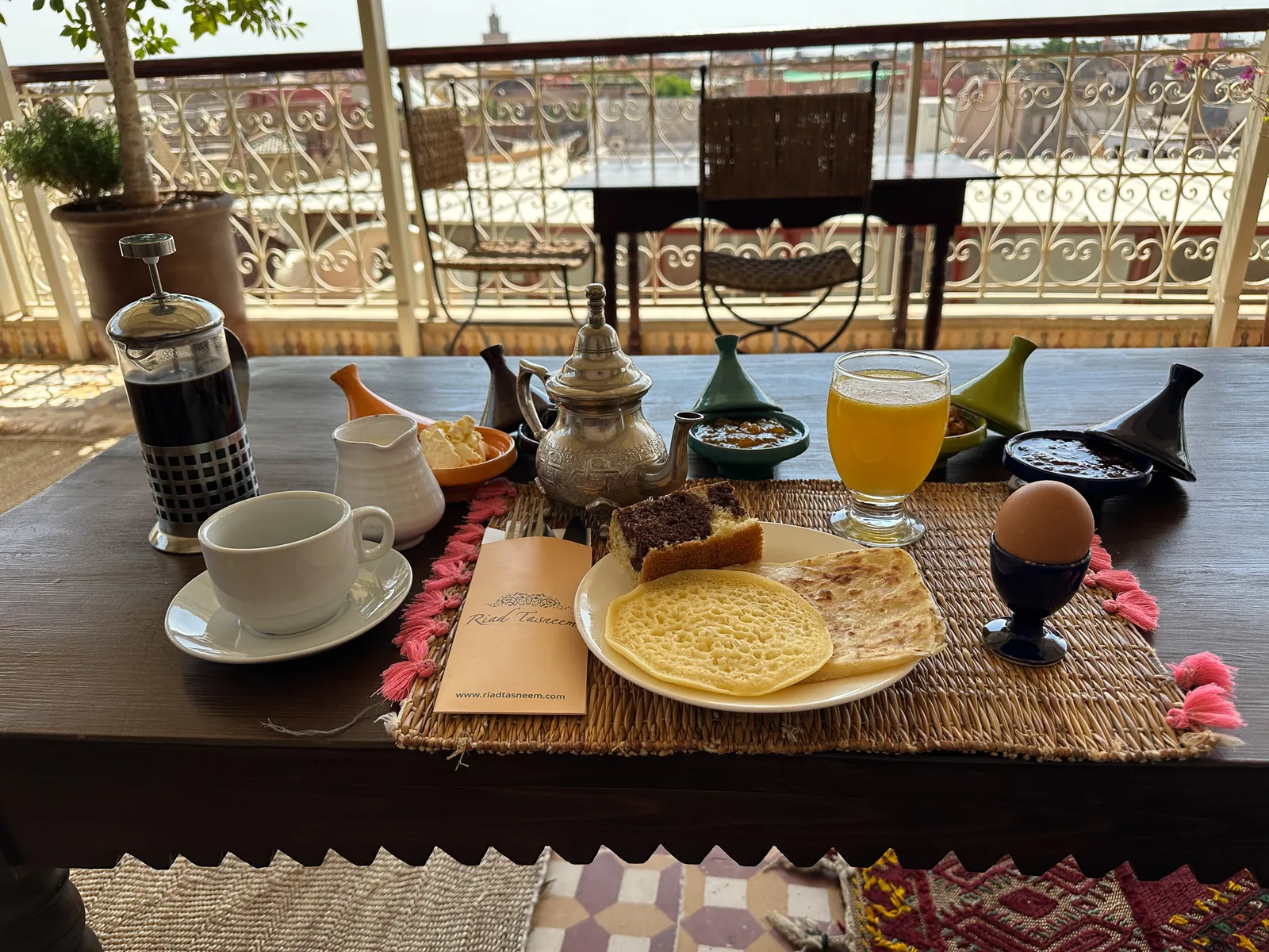 Moroccan breakfast at Riad Tasneem from above: baghrir and msemen, olives, jams in mini tagines, orange juice, egg and coffee on a Riad Tasneem placemat