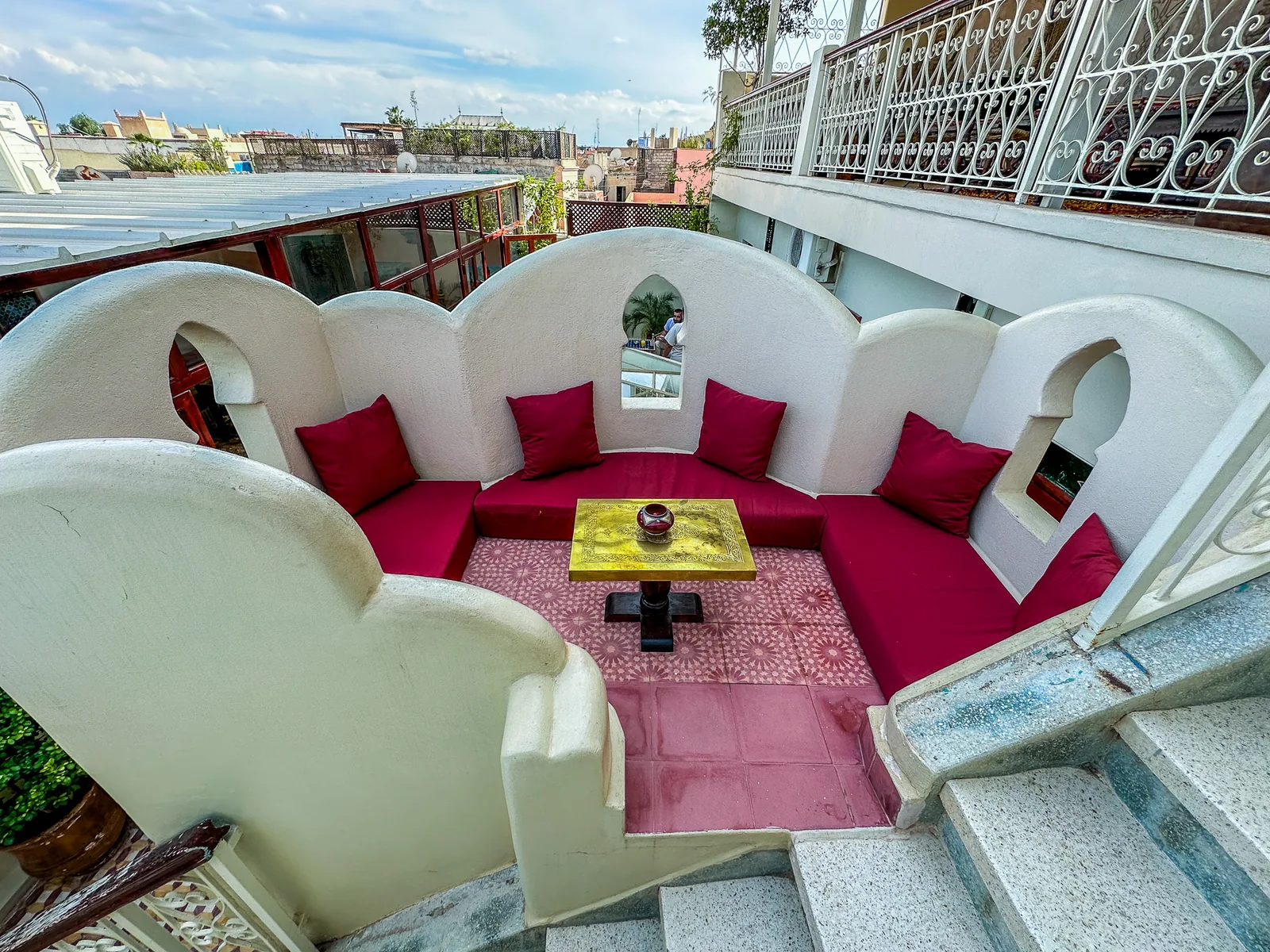 A small lounge corner on the terrace of Riad Tasneem: sculpted white arches, red cushions and a brass table, open to the sky over the medina