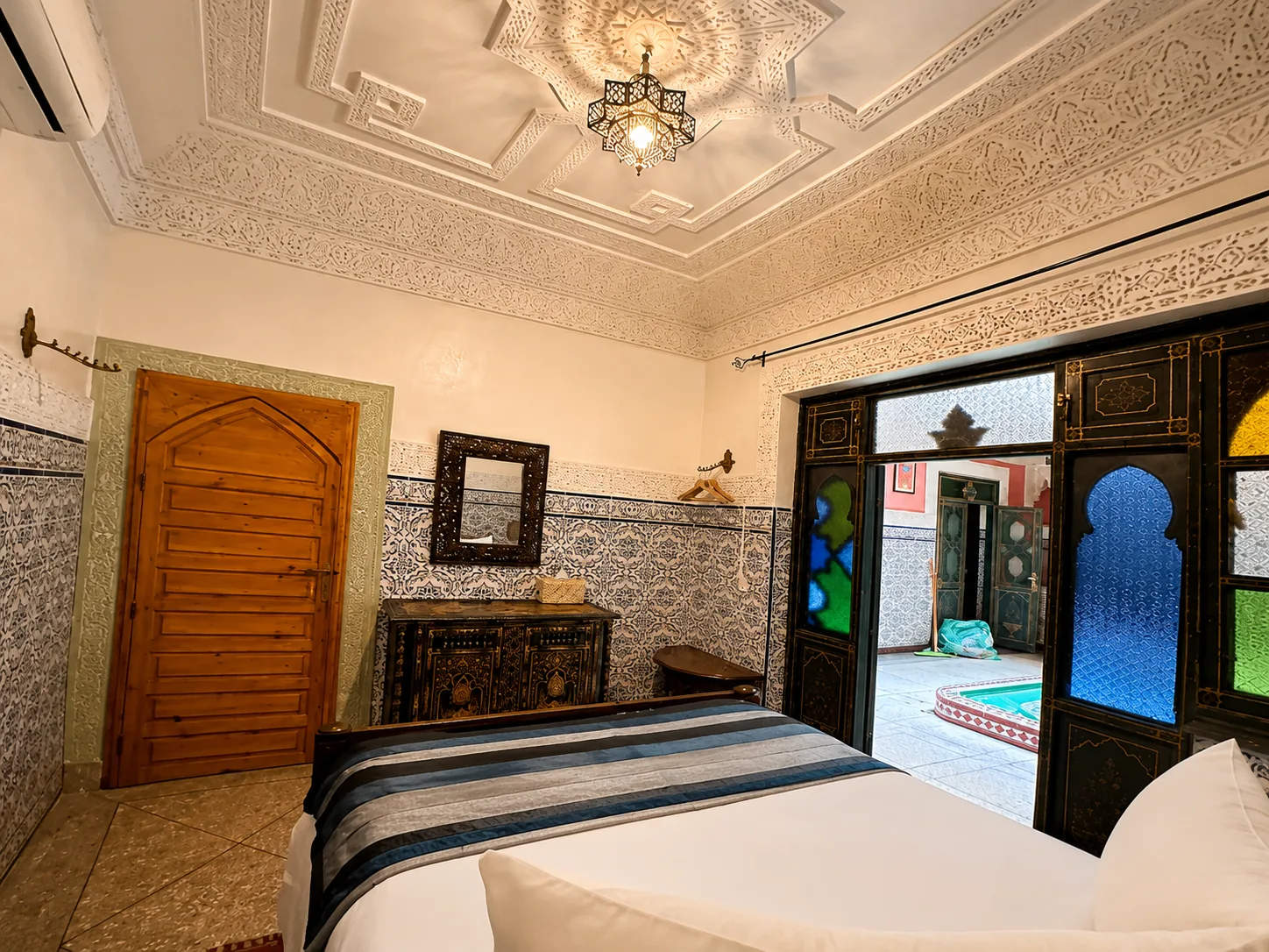 Laila room: wide angle view showing the intricately carved stucco ceiling, oriental lamp, carved cabinet with mirror and the stained-glass door to the patio